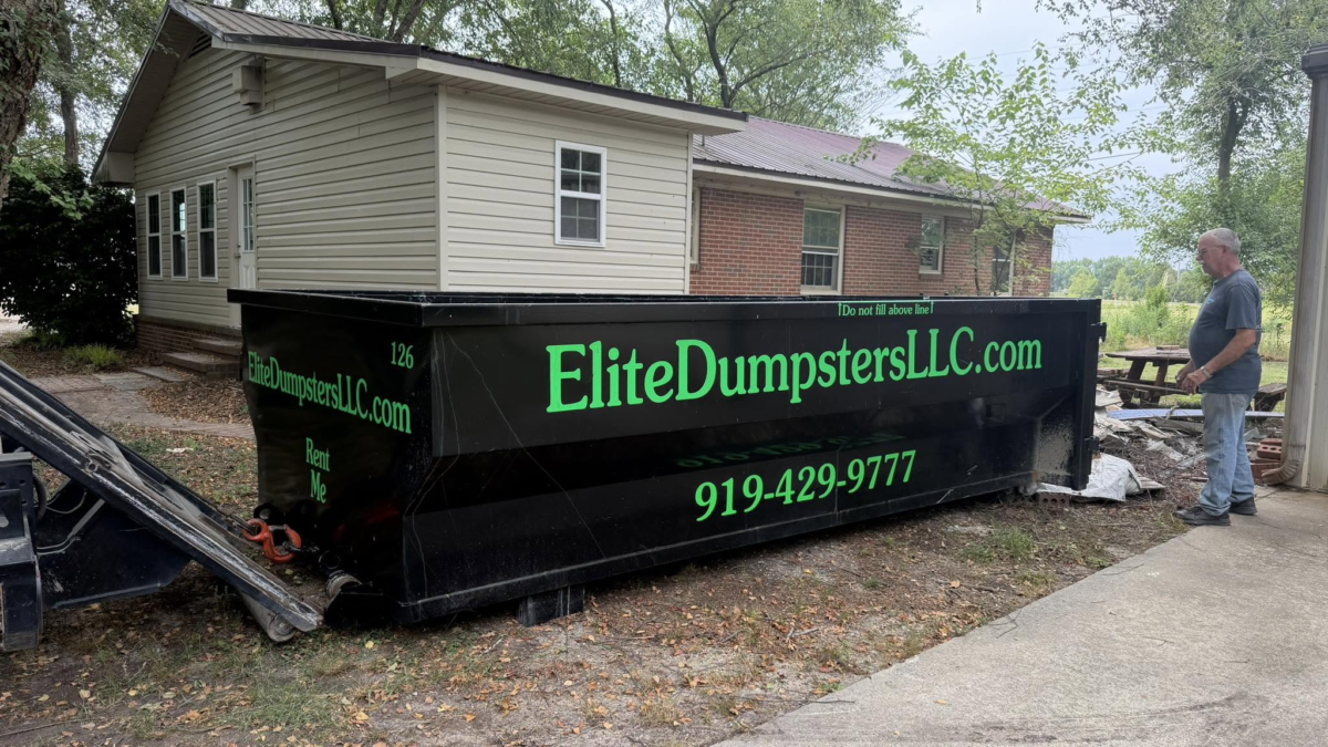 A person standing next to a dumpster outside a house