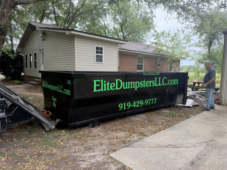A person standing next to a dumpster outside a house